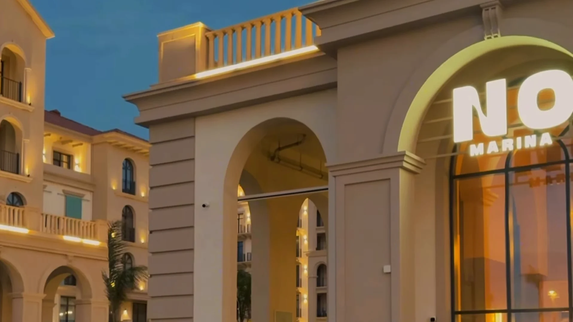 Фасад дома в Marina Village в сумерках: горящая вывеска NO MARINA над арочным входом. Кадр ролика @n0marina «The End of Summer», 01.09.2026
